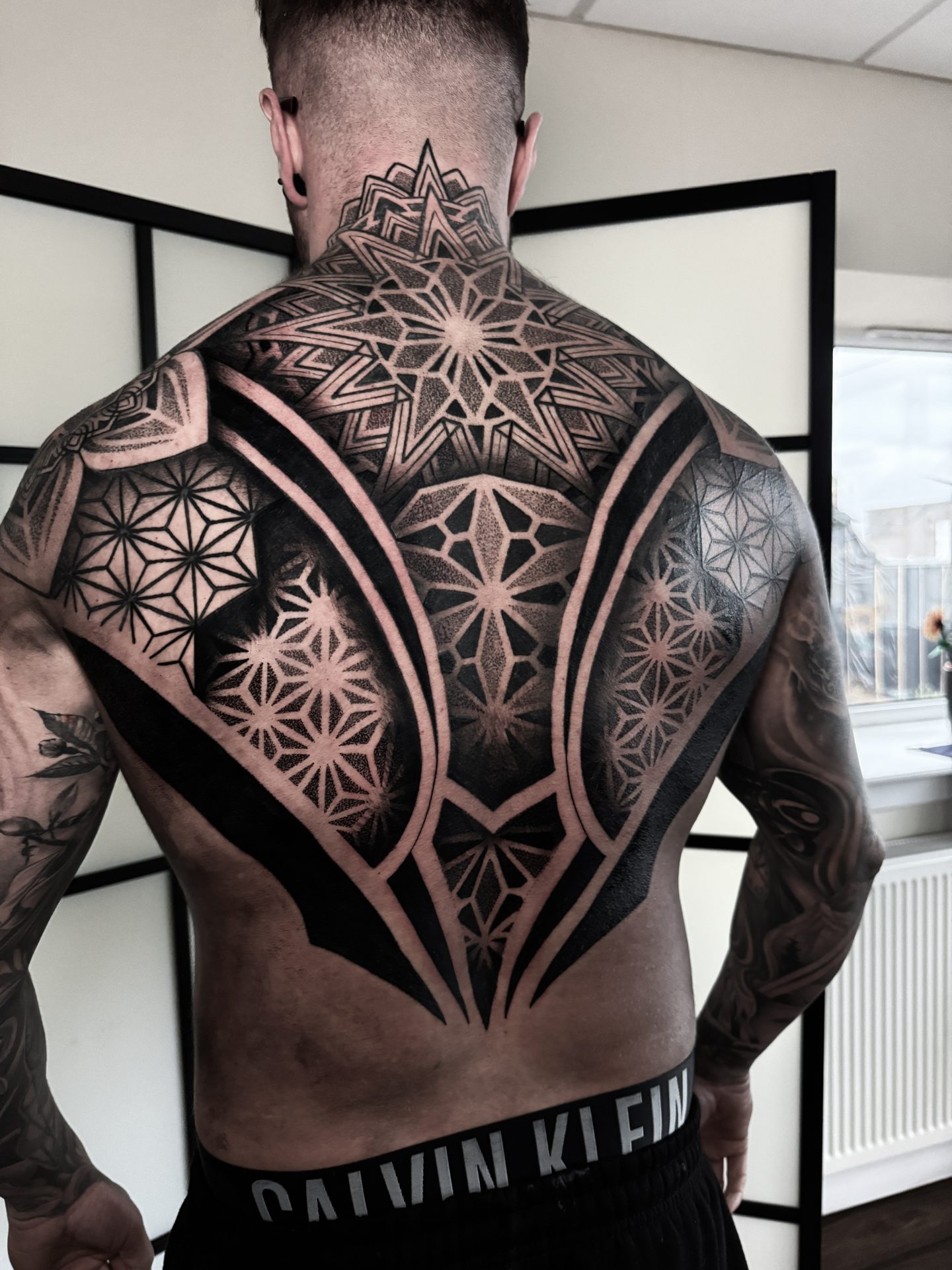 Large geometric back piece with winged motif by Liam Couper