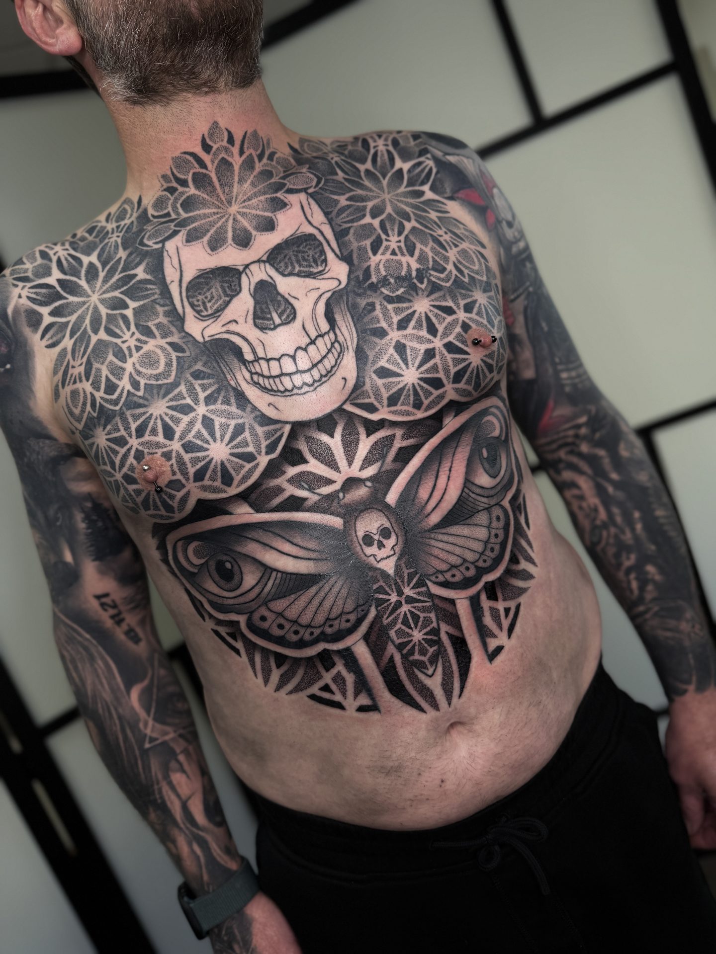 Front view of a geometric skull chest piece and sleeves by Liam Couper